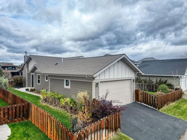 exterior space featuring aphalt driveway, roof with shingles, board and batten siding, a garage, and fence private yard