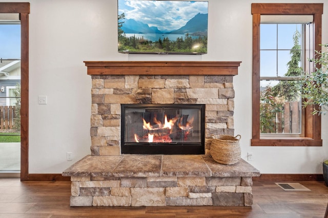 room details with visible vents, a stone fireplace, baseboards, and wood finished floors