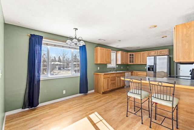 kitchen featuring light wood-style flooring, a sink, baseboards, stainless steel fridge with ice dispenser, and glass insert cabinets