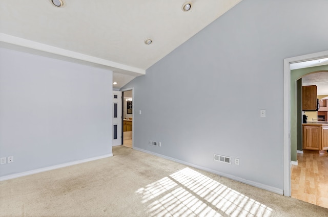 empty room with arched walkways, lofted ceiling, visible vents, light carpet, and baseboards