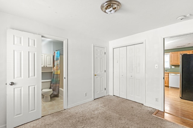 unfurnished bedroom featuring light carpet, baseboards, ensuite bathroom, and freestanding refrigerator