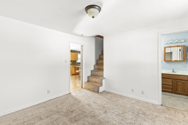 unfurnished room with light colored carpet, a sink, stairway, and baseboards