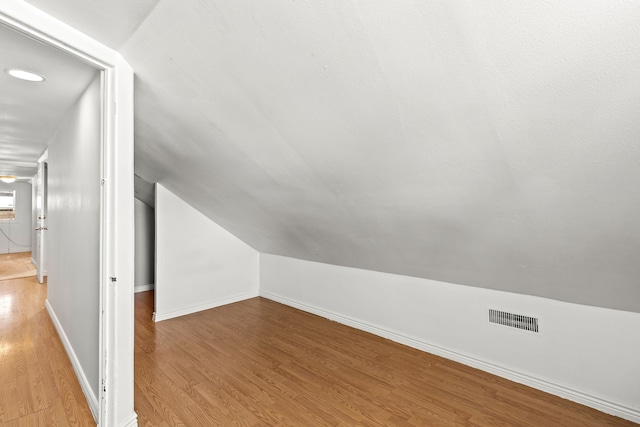 bonus room featuring baseboards, visible vents, vaulted ceiling, and wood finished floors