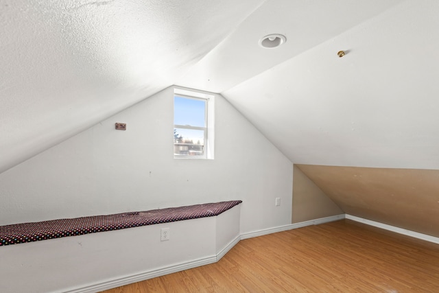 additional living space with light wood-type flooring, lofted ceiling, baseboards, and a textured ceiling