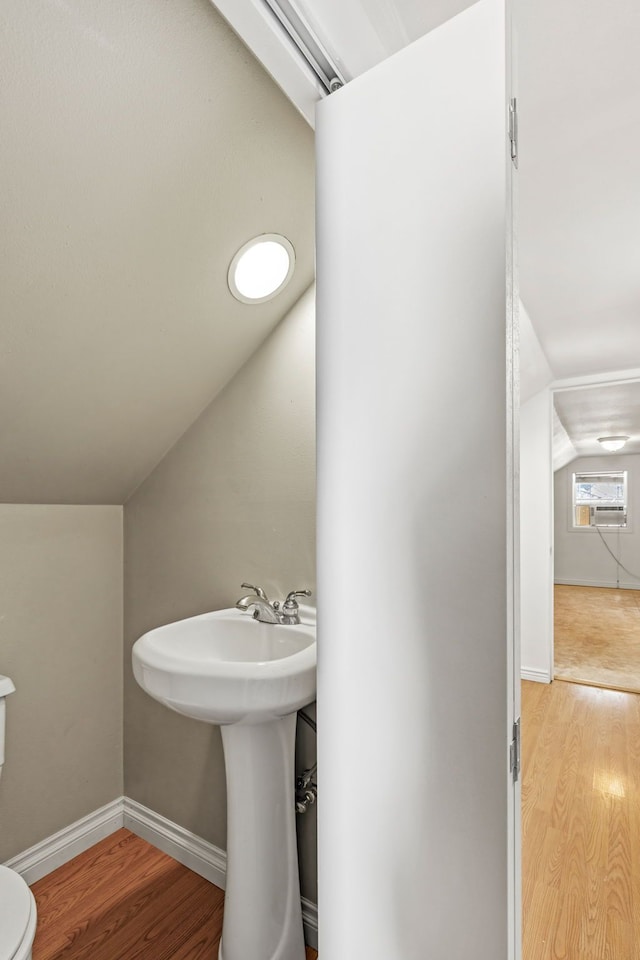 half bathroom featuring vaulted ceiling, wood finished floors, toilet, and baseboards