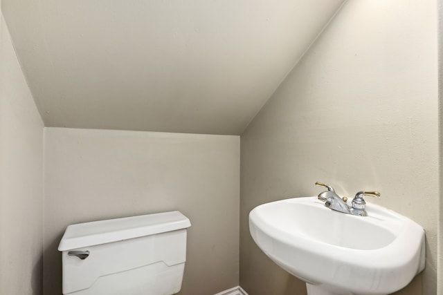 bathroom featuring toilet, a sink, and lofted ceiling