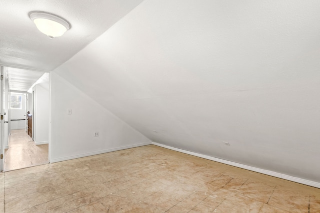 bonus room featuring vaulted ceiling, a textured ceiling, and baseboards