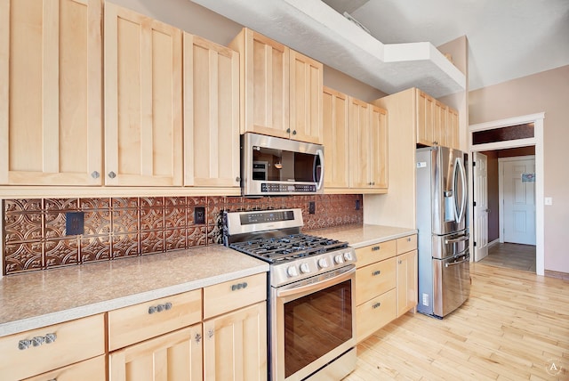 kitchen featuring light brown cabinets, stainless steel appliances, light wood-style floors, light countertops, and tasteful backsplash