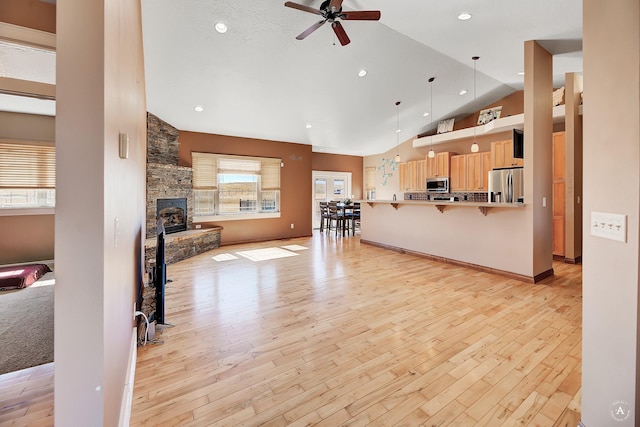 living room featuring light wood finished floors, baseboards, lofted ceiling, ceiling fan, and a stone fireplace