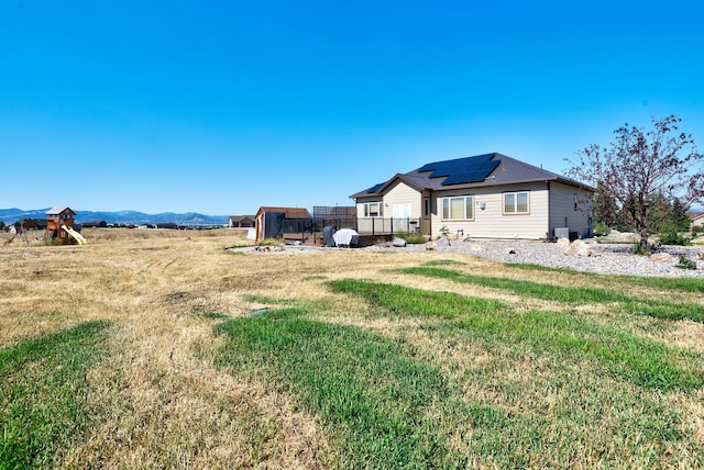 back of house featuring a yard, a playground, a mountain view, and roof mounted solar panels