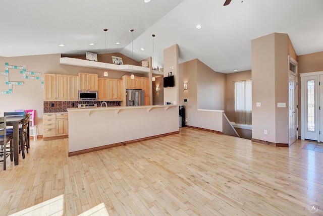 kitchen featuring appliances with stainless steel finishes, a kitchen breakfast bar, hanging light fixtures, light wood-style floors, and light brown cabinets