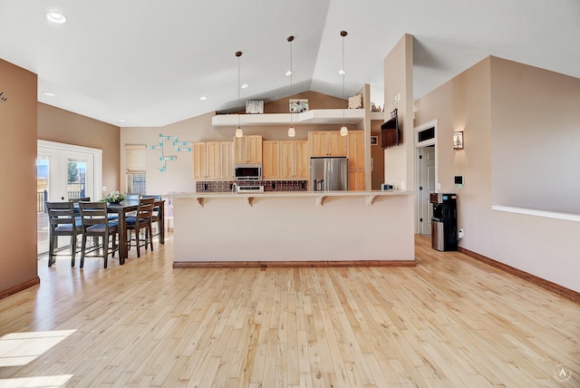 kitchen featuring light wood finished floors, a breakfast bar area, hanging light fixtures, light brown cabinetry, and appliances with stainless steel finishes