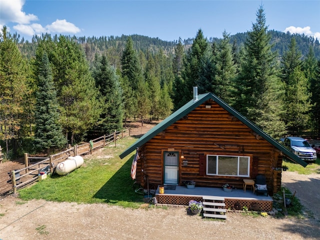 log home with a forest view, fence, a front lawn, and log exterior