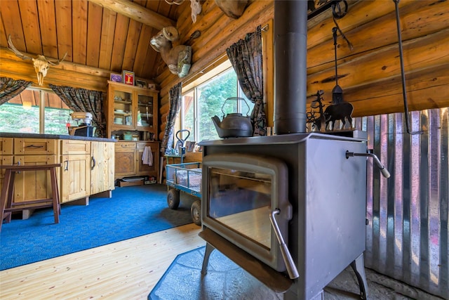 interior space with a wealth of natural light, wooden ceiling, log walls, and a wood stove