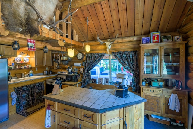 kitchen featuring tile counters, stainless steel appliances, rustic walls, wood ceiling, and a sink