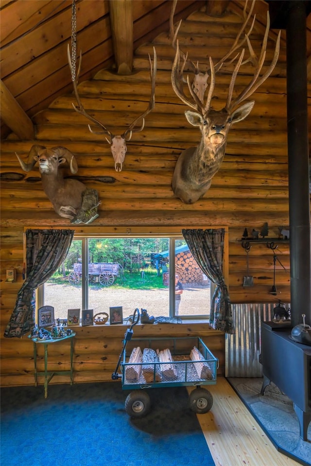 interior space featuring log walls, high vaulted ceiling, wood finished floors, and a wood stove