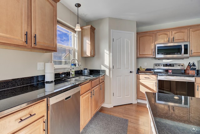 kitchen with light wood-style flooring, stainless steel appliances, a sink, dark stone countertops, and decorative light fixtures