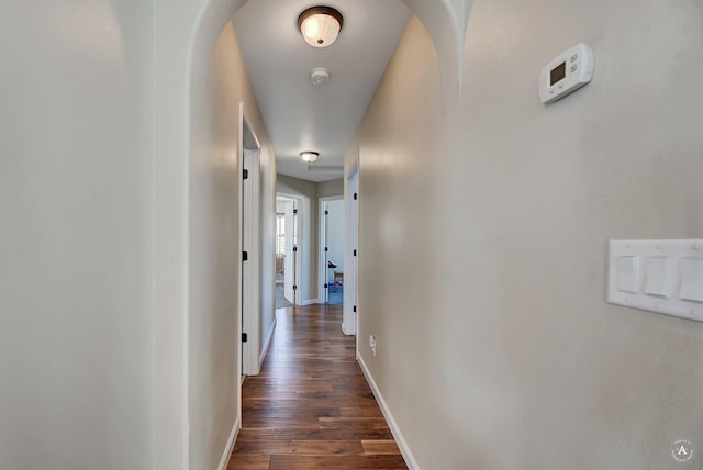 corridor with arched walkways, dark wood-style flooring, and baseboards