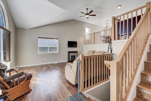 living area with baseboards, a glass covered fireplace, dark wood-style floors, stairs, and high vaulted ceiling