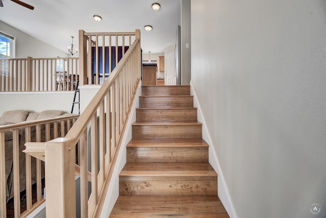 stairs featuring ceiling fan with notable chandelier, wood finished floors, and baseboards