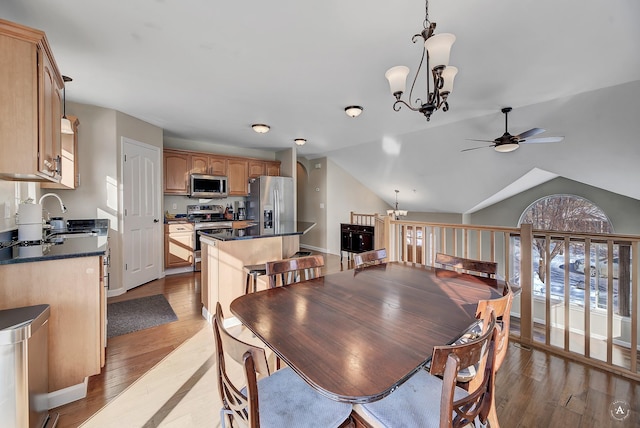 dining room with lofted ceiling, ceiling fan with notable chandelier, light wood-style flooring, and baseboards