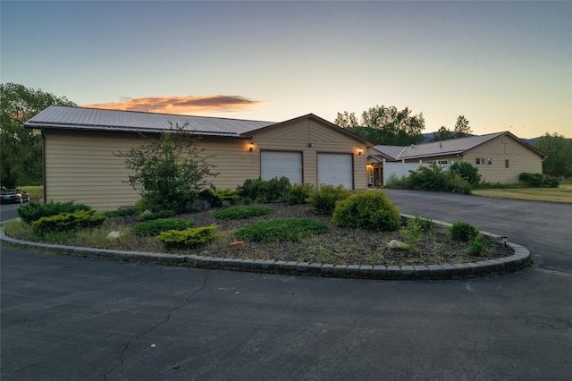 ranch-style house featuring a garage, metal roof, and aphalt driveway