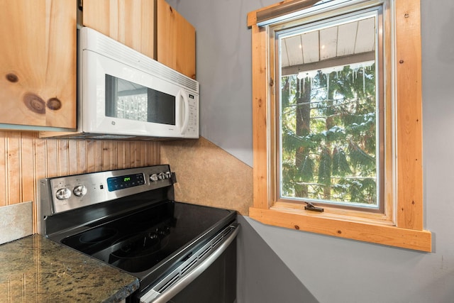 kitchen featuring stainless steel range with electric stovetop, dark stone counters, a healthy amount of sunlight, and white microwave