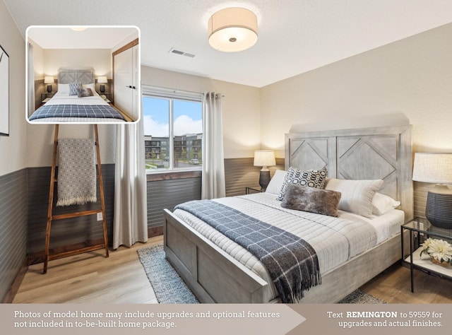 bedroom featuring light wood-type flooring, wainscoting, and visible vents