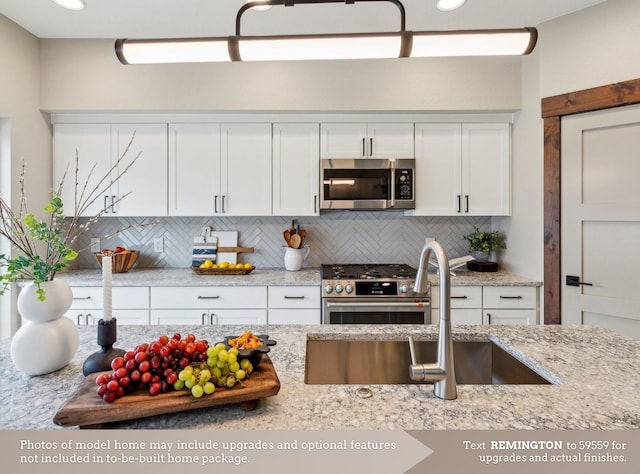 kitchen featuring backsplash, light stone countertops, stainless steel appliances, white cabinetry, and a sink