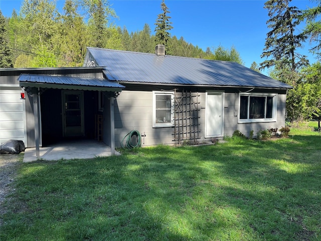 back of house with metal roof and a lawn