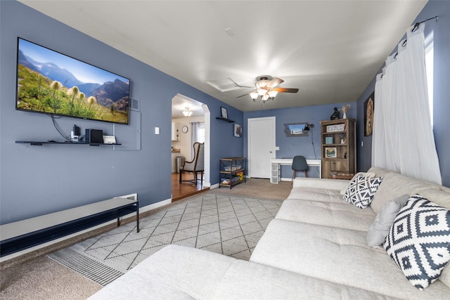 living room with light carpet, baseboards, arched walkways, and a ceiling fan