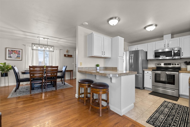 kitchen with light wood finished floors, stainless steel appliances, white cabinets, a peninsula, and a kitchen breakfast bar