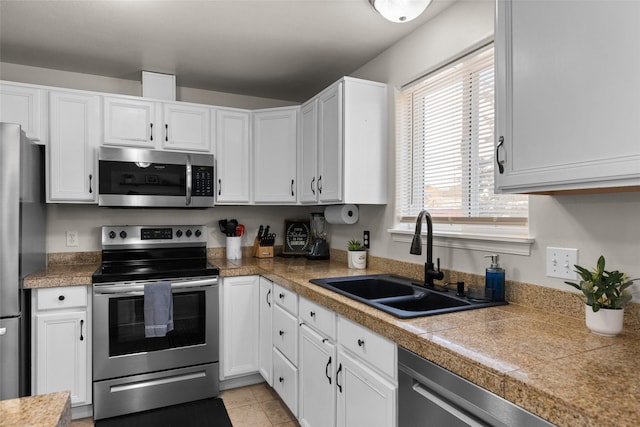 kitchen featuring stainless steel appliances, tile counters, white cabinetry, a sink, and light tile patterned flooring