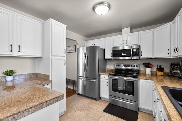 kitchen featuring stainless steel appliances, a sink, tile counters, and white cabinetry