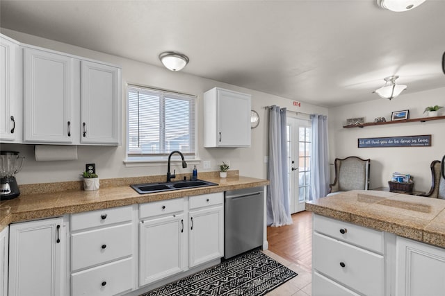 kitchen with stainless steel dishwasher, a sink, tile counters, and white cabinetry