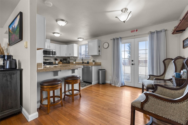 kitchen with a peninsula, light wood finished floors, white cabinetry, and appliances with stainless steel finishes