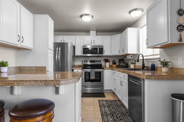 kitchen featuring tile countertops, appliances with stainless steel finishes, a kitchen bar, and white cabinets