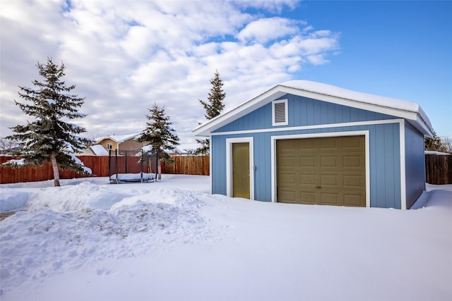 snow covered garage with a detached garage and fence