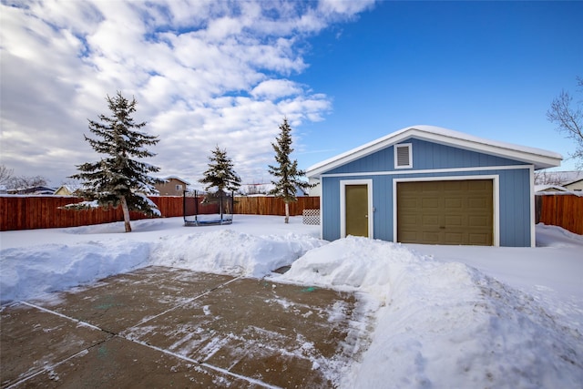 snowy yard with a garage, fence, and an outbuilding