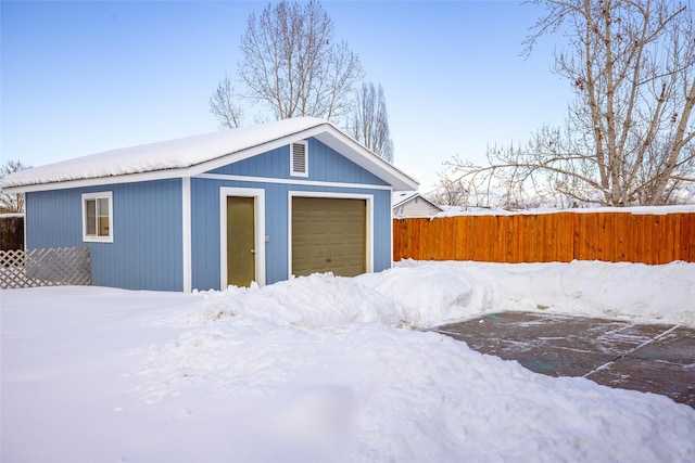 snow covered garage featuring a detached garage and fence