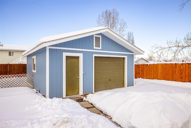 snow covered structure featuring an outdoor structure and fence