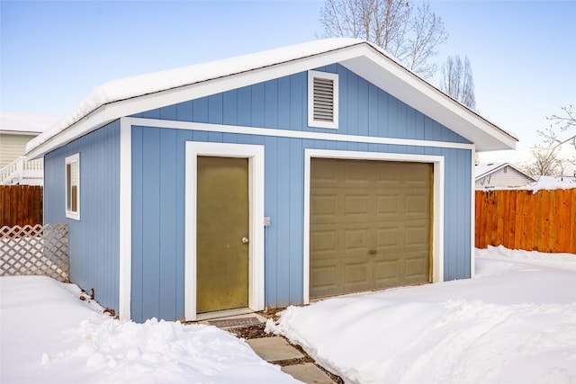 snow covered garage with a detached garage and fence