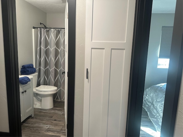 full bathroom with a textured ceiling, curtained shower, toilet, wood finished floors, and vanity