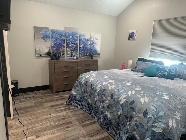 bedroom featuring lofted ceiling, wood finished floors, and baseboards