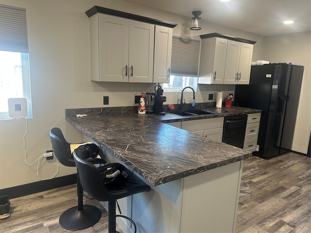 kitchen featuring white cabinets, wood finished floors, a peninsula, black appliances, and a sink