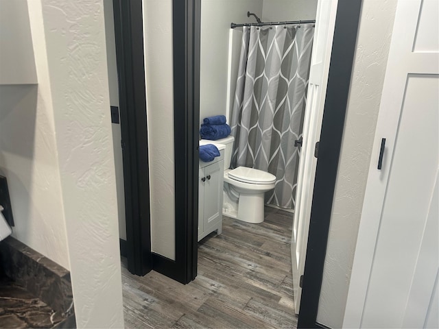 bathroom featuring curtained shower, a textured wall, toilet, and wood finished floors