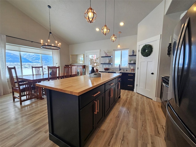 kitchen featuring open shelves, butcher block counters, freestanding refrigerator, light wood-type flooring, and dark cabinetry