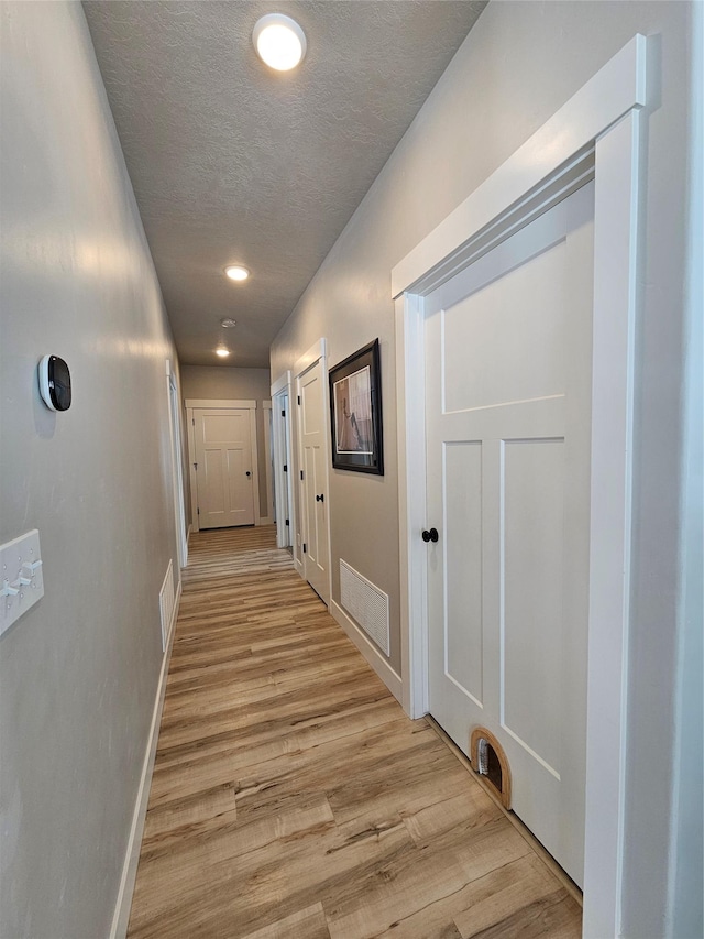 corridor with baseboards, visible vents, light wood-style flooring, and a textured ceiling