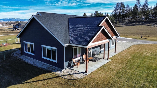 back of property featuring a patio area, roof with shingles, a mountain view, and a yard