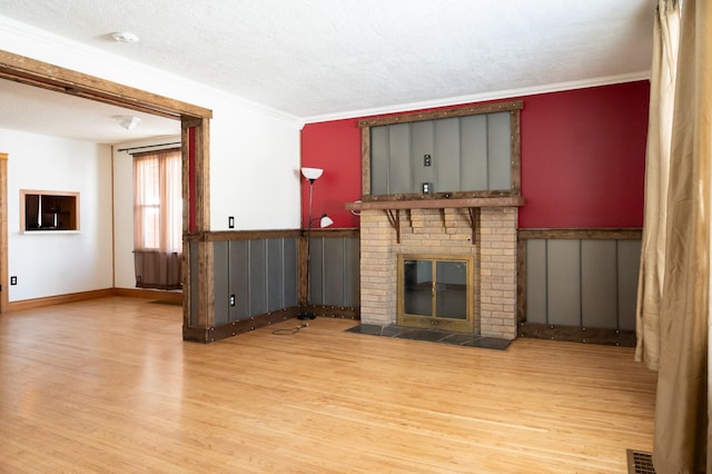 unfurnished living room with wainscoting, wood finished floors, a textured ceiling, crown molding, and a fireplace